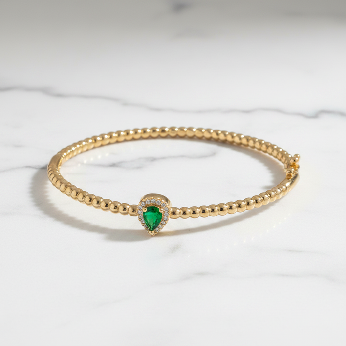 Gold bracelet with a green gemstone on a marble surface
