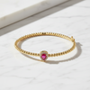 Gold bracelet with a heart-shaped red gemstone on a white marble surface