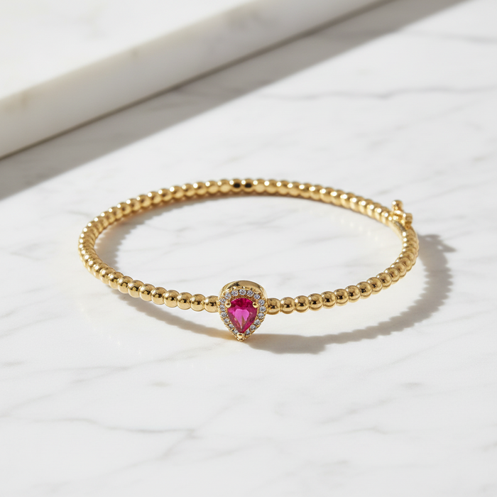 Gold bracelet with a heart-shaped red gemstone on a white marble surface