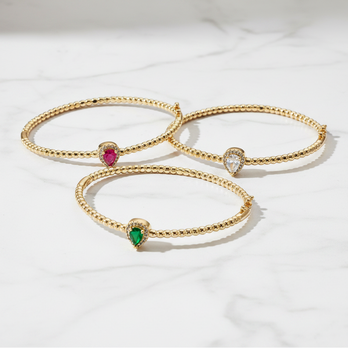 Three gold bracelets with gemstones on a white background