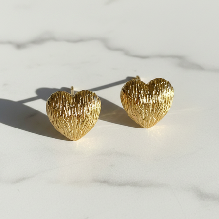 Gold heart-shaped earrings on a light marble background
