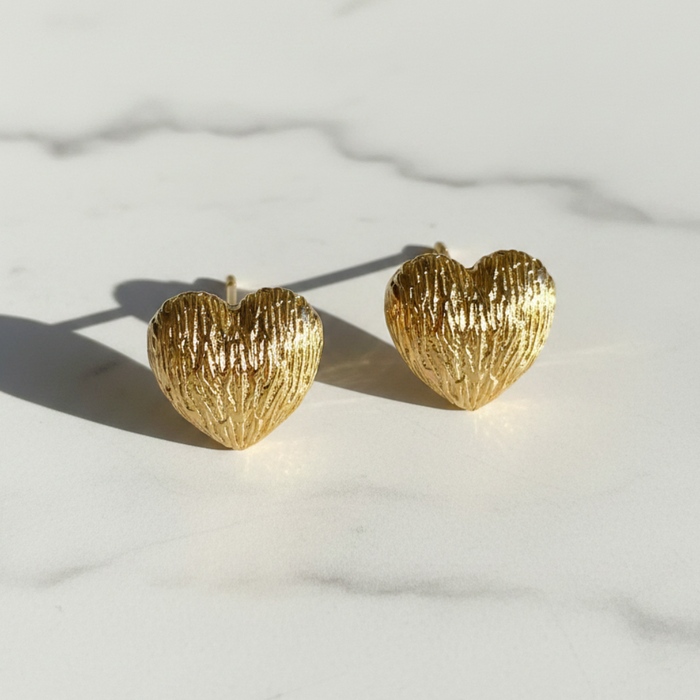 Gold heart-shaped earrings on a light marble background