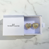 Gold heart-shaped earrings in a box with 'The Christy F Collection' branding on a marble surface.
