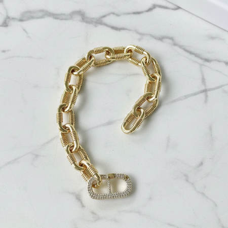 Gold chain bracelet with a heart-shaped charm on a marble surface