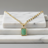 Gold necklace with a green pendant on a marble surface