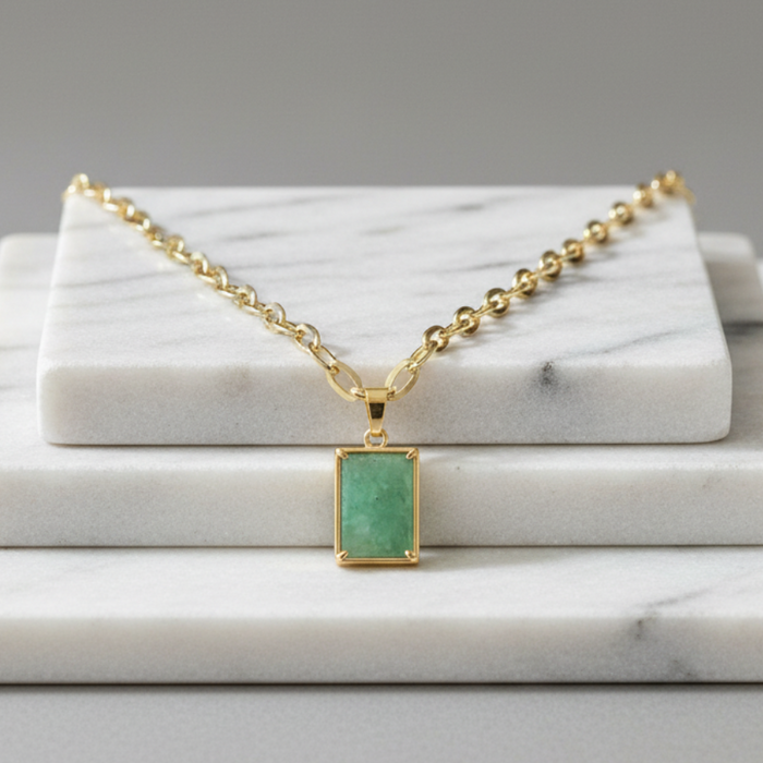 Gold necklace with a green pendant on a marble surface