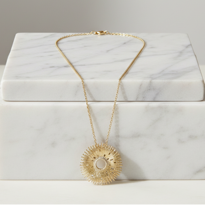 Gold necklace with a sunflower pendant on a marble box
