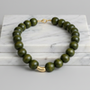 Green beaded necklace with gold clasp on a marble surface