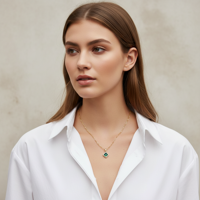 Woman wearing a gold necklace with a green gemstone on a neutral background
