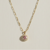 Gold necklace with a pink pendant on a beige book