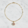 Gold necklace with a pink pendant on a marble surface