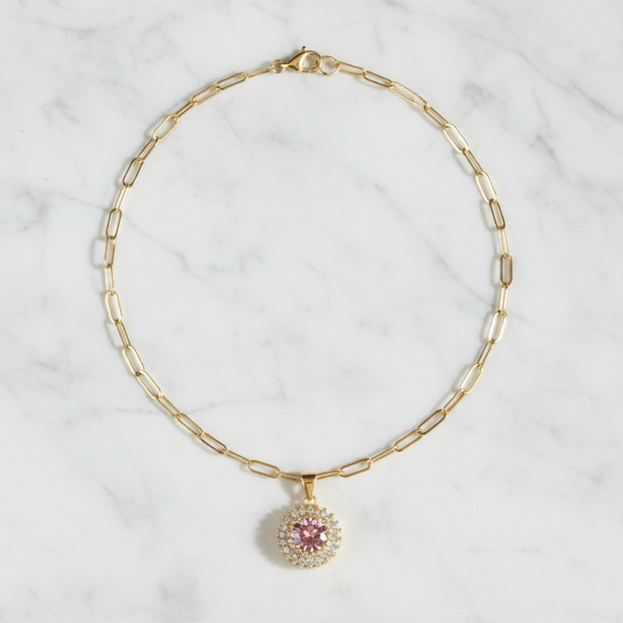 Gold necklace with a pink pendant on a marble surface