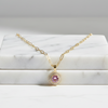 Gold necklace with a pink gemstone pendant on a marble surface