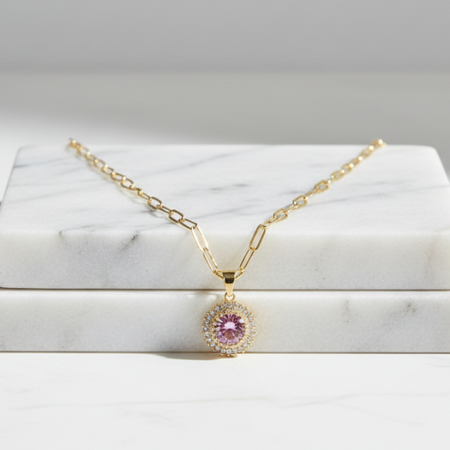 Gold necklace with a pink gemstone pendant on a marble surface