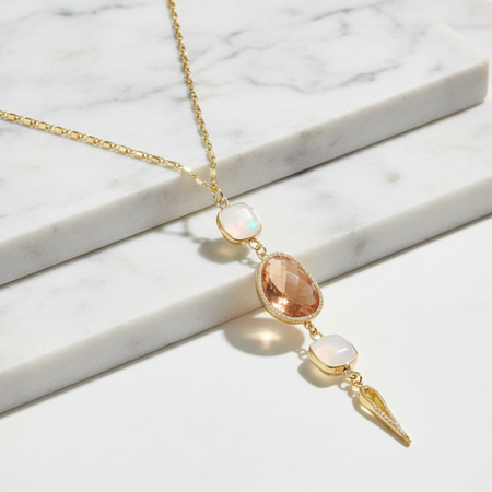Gold necklace with opal and peach-colored stones on a marble surface