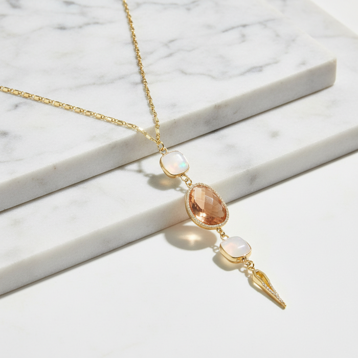 Gold necklace with opal and peach-colored stones on a marble surface