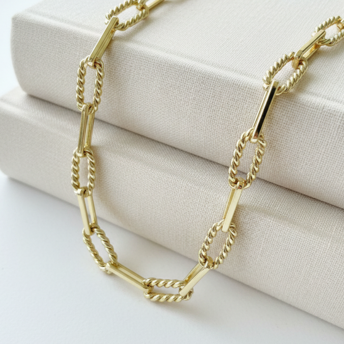 Gold chain necklace on a textured beige surface