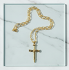 Gold chain necklace with a cross pendant on a marble surface