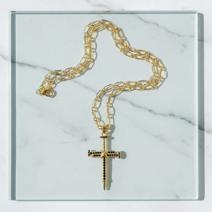 Gold chain necklace with a cross pendant on a marble surface