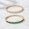 Two gold bangles with gemstones on a white fabric background