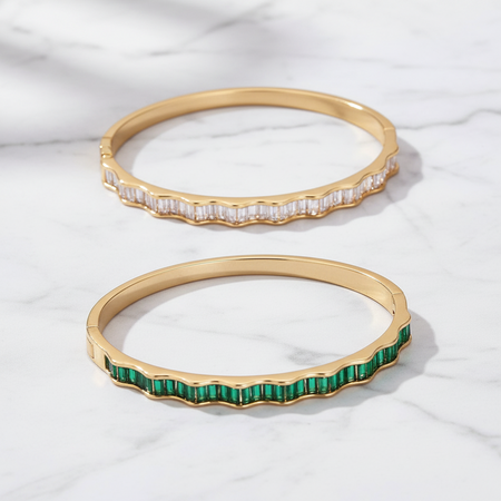 Two gold bangles with gemstones on a white fabric background