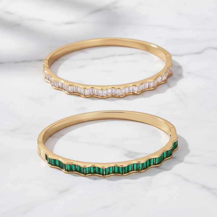Two gold bangles with gemstones on a white fabric background