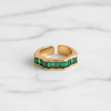 Gold ring with green gemstones on a white fabric background