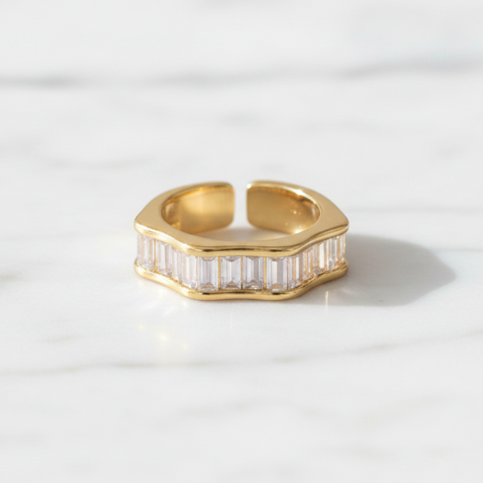 Gold ring with baguette cut gemstones on a light gray background