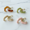 Four pairs of hoop earrings in different colors on a marble surface
