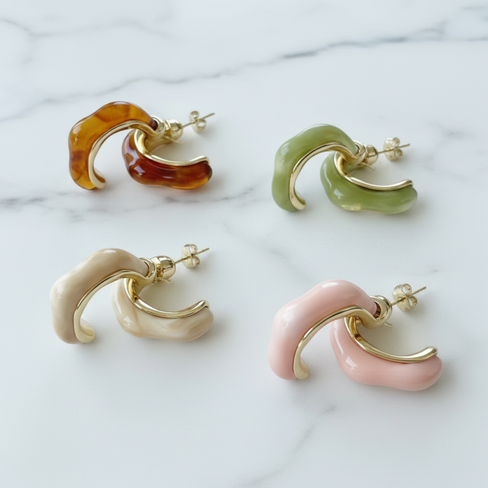 Four pairs of hoop earrings in different colors on a marble surface