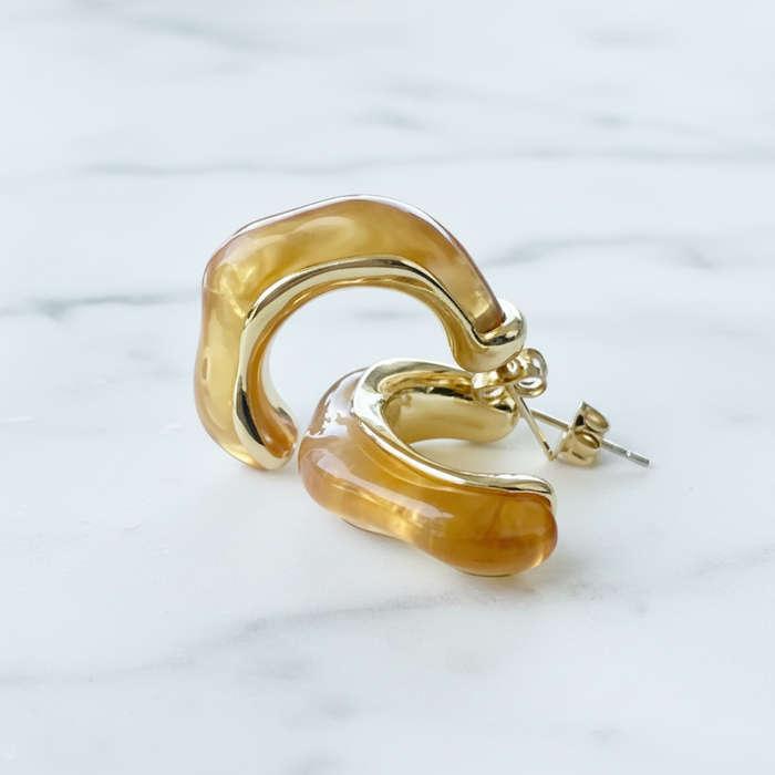 Gold hoop earrings with amber-colored stones on a marble background