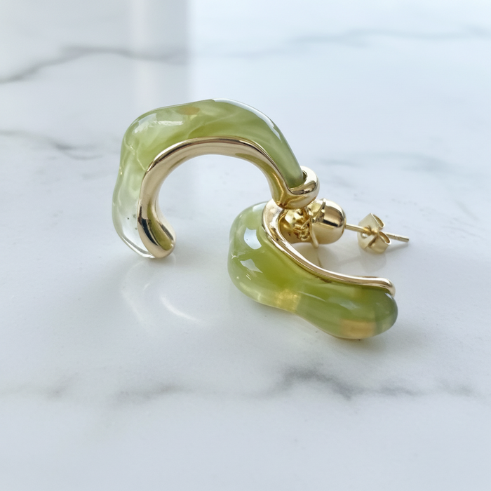 Green stone earring with gold setting on a marble background
