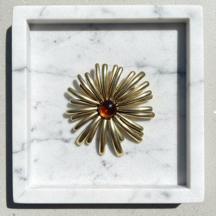 Gold brooch with a central gemstone on a marble surface