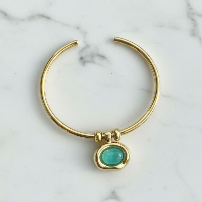 Gold bracelet with a green gemstone on a marble background