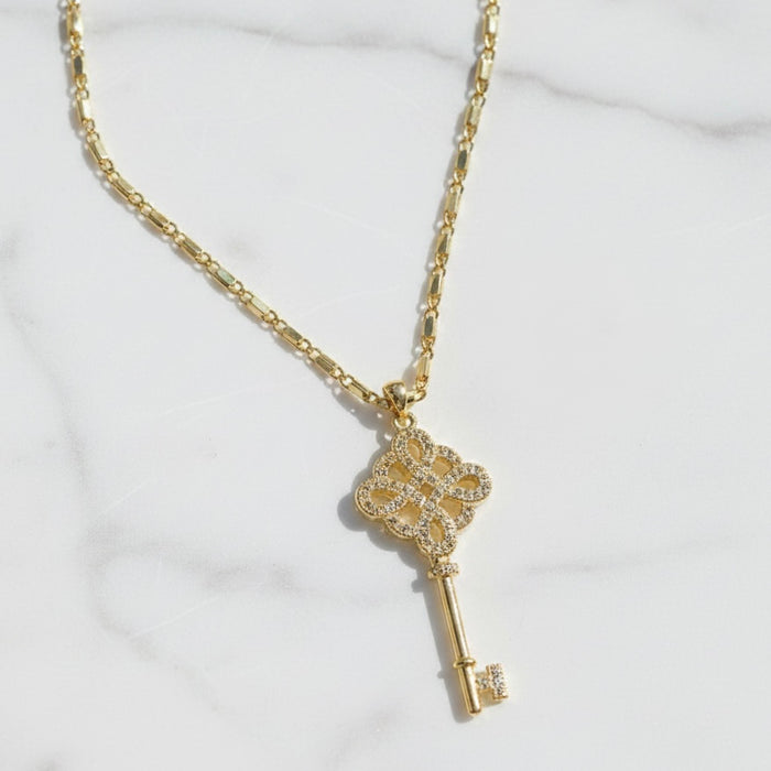 Gold key-shaped pendant necklace on a white background