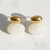 Gold and white earrings on a light background