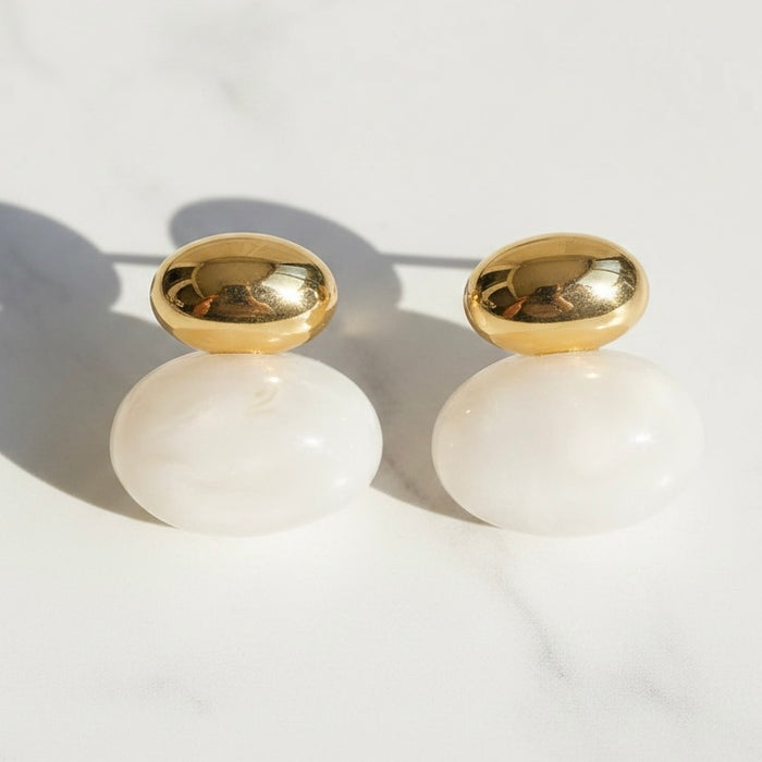 Gold and white earrings on a light background