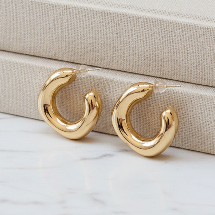 Gold hoop earrings on a marble surface with a beige jewelry box in the background.