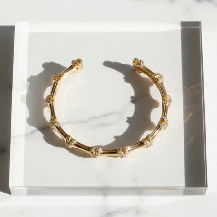 Gold bracelet on a clear stand with a marble background