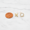 Two gold earrings next to a penny on a white fabric background
