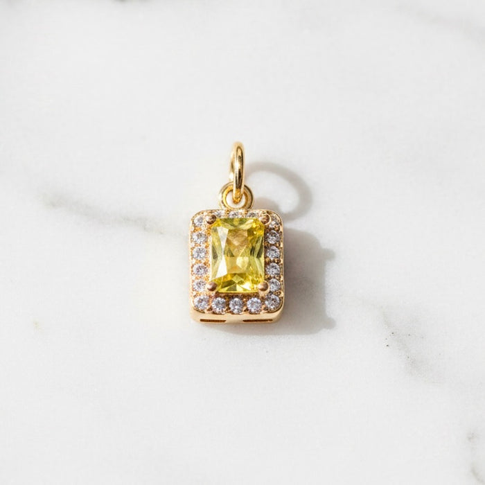 Gold pendant with a yellow gemstone on a white marble background