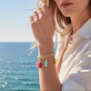 Woman wearing a gold bracelet with colorful charms by the ocean