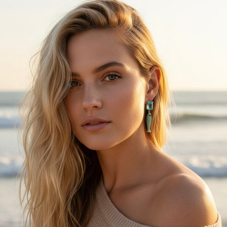 Woman with long blonde hair wearing a beige off-shoulder sweater on a beach.