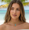 Woman wearing a gold necklace with a blue pendant on a beach