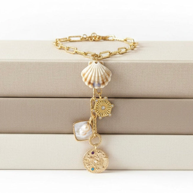 Gold necklace with shell and coin charms on a beige jewelry box