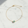 Gold bracelet with a green gemstone on a marble surface