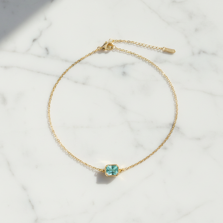 Gold bracelet with a green gemstone on a marble surface