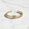Gold bracelet with a central emerald stone on a white fabric background