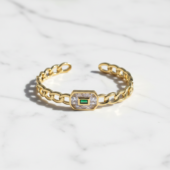 Gold bracelet with a central emerald stone on a white fabric background