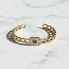 Gold bracelet with a central gemstone on a marble background